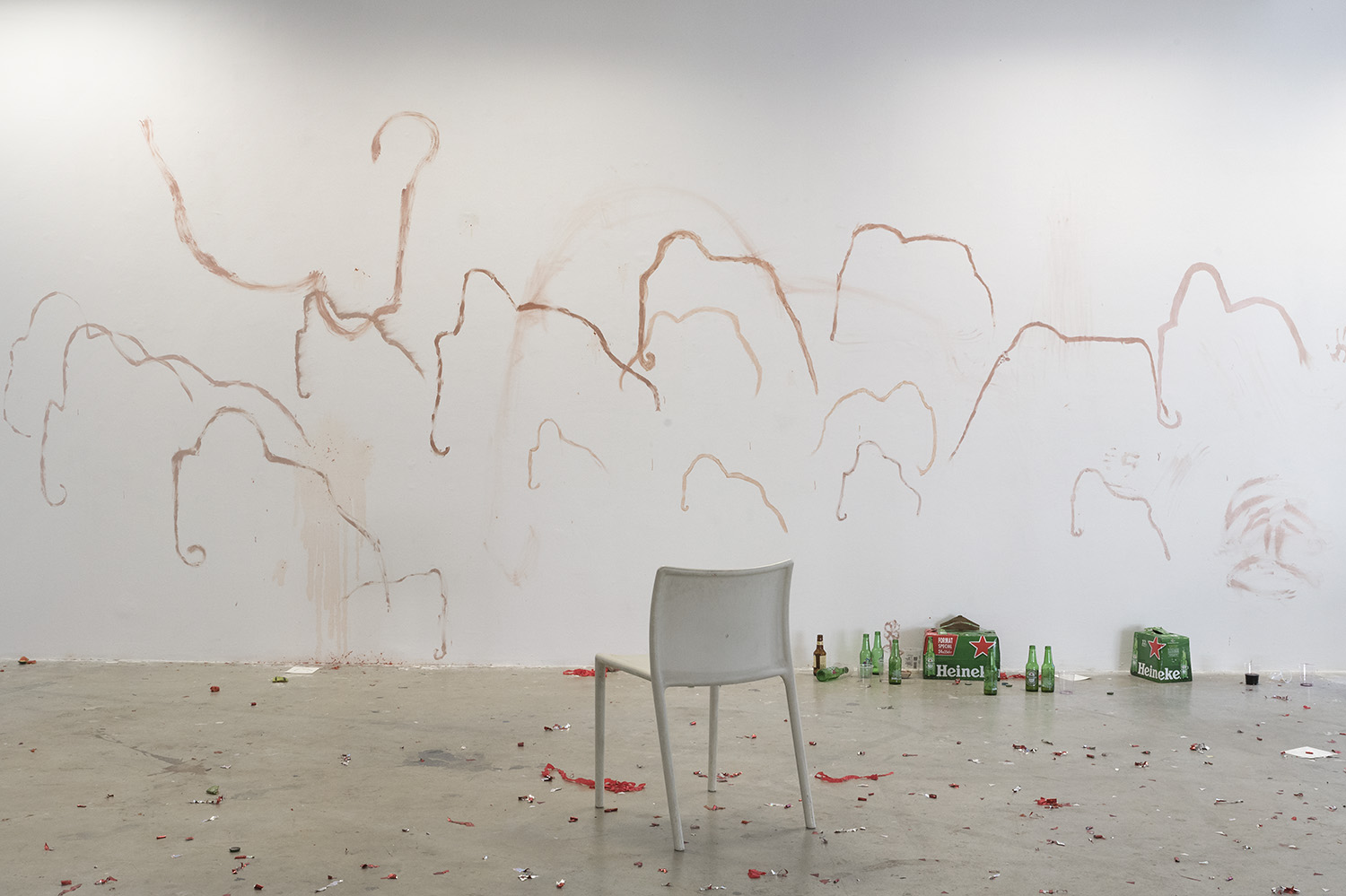 photo du lendemain : un mur est recuvert de dessins de mammouth, plusieurs packs de bières et bouteilles vides sont au milieu des cotillons, une chaise est seule au milieu de la salle.